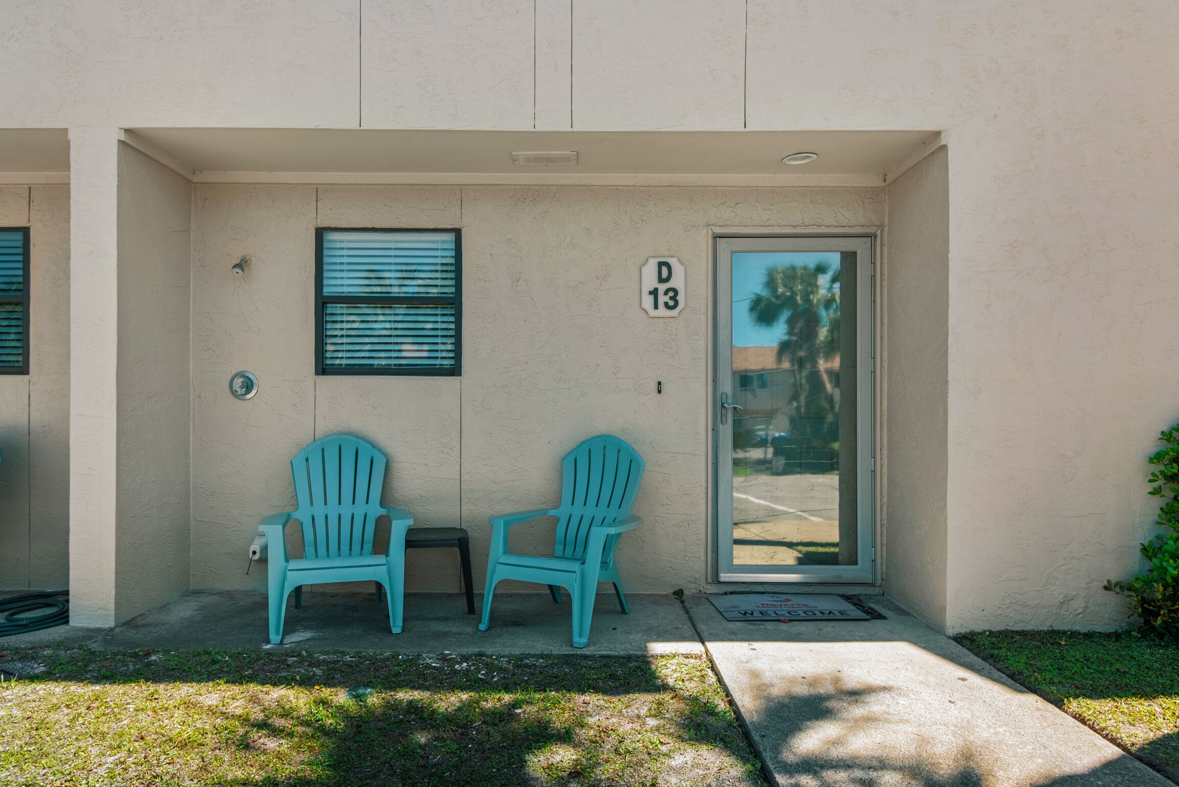 A building entrance with two turquoise chairs, a door marked "D 13", and a window with blinds.