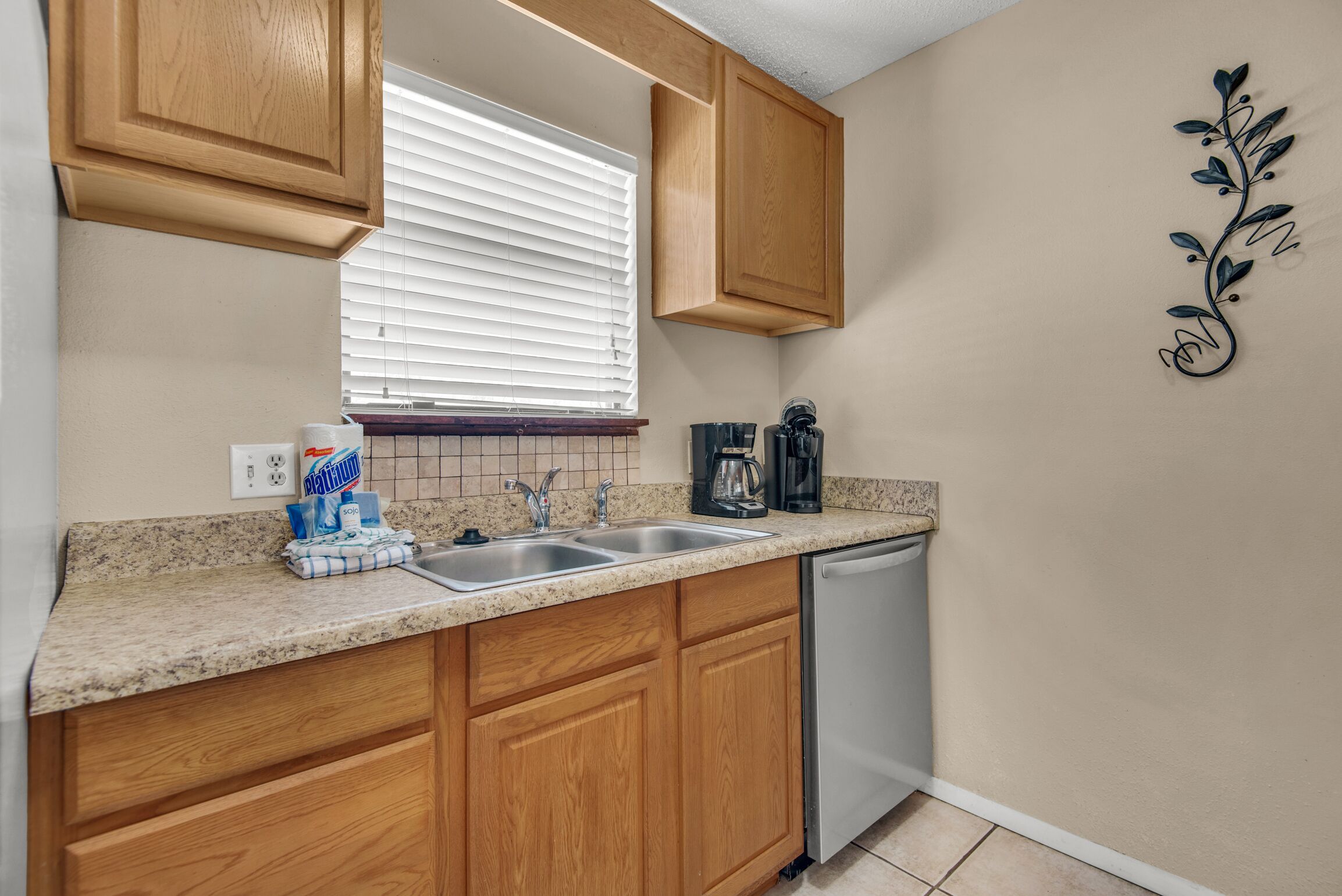 A kitchen with wooden cabinets, a double sink, a coffee maker, and a dishwasher.