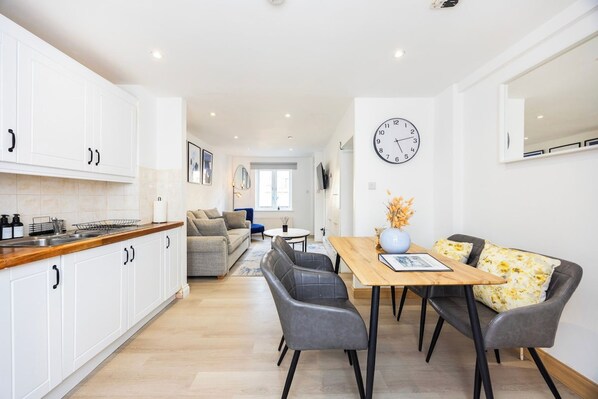 Une cuisine moderne avec des meubles blancs, un plan de travail en bois et un coin repas comprenant une table en bois et des chaises grises.