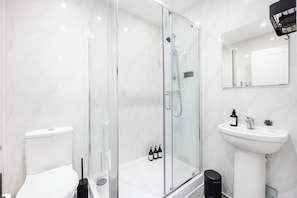 A modern bathroom with a glass-enclosed shower, a white sink, and a toilet.