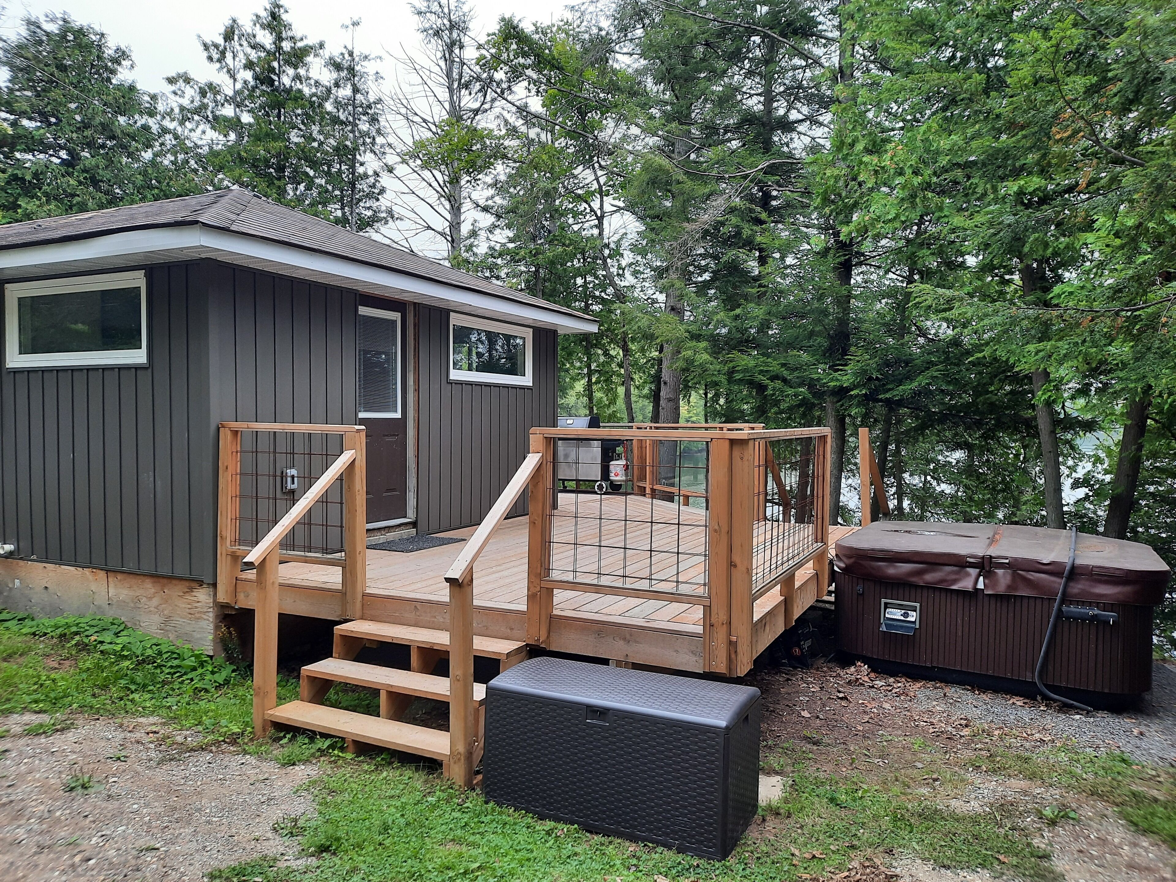 A small cabin with a wooden deck and a hot tub.
