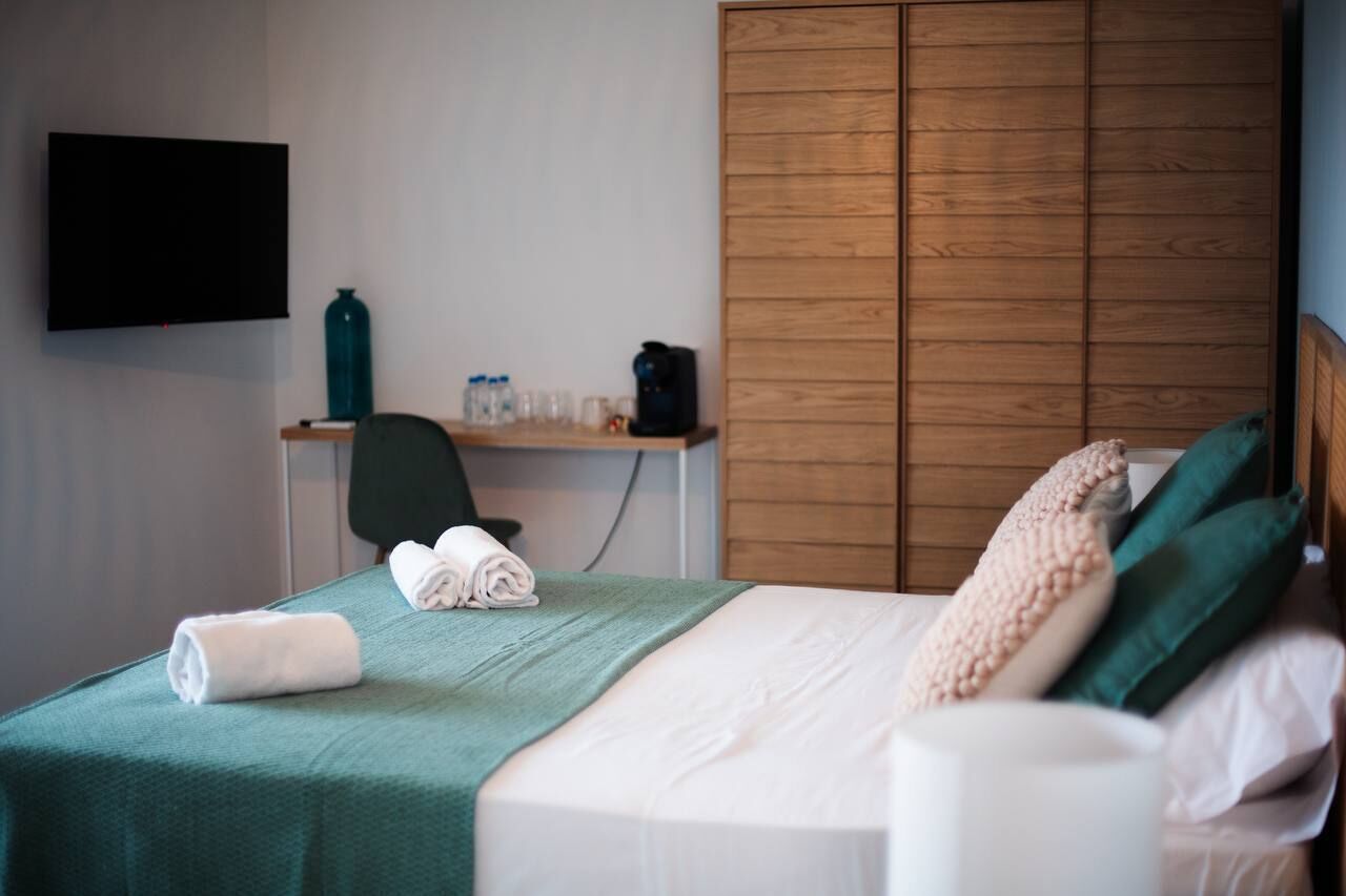 A hotel room with a bed, a desk with a chair, a television, and a wardrobe.