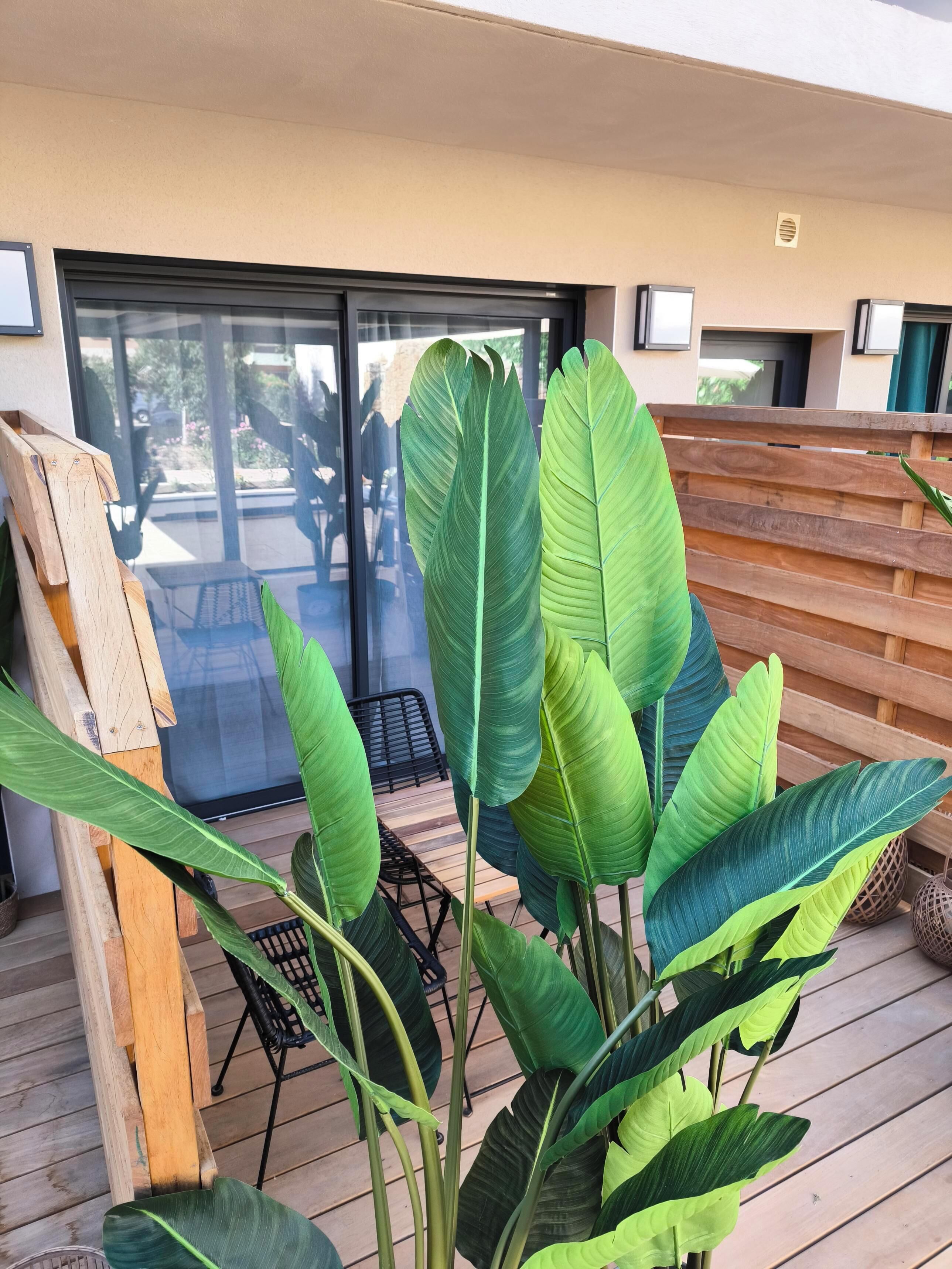 Um deck de madeira com plantas verdes grandes, uma porta de vidro e um cercado de madeira.