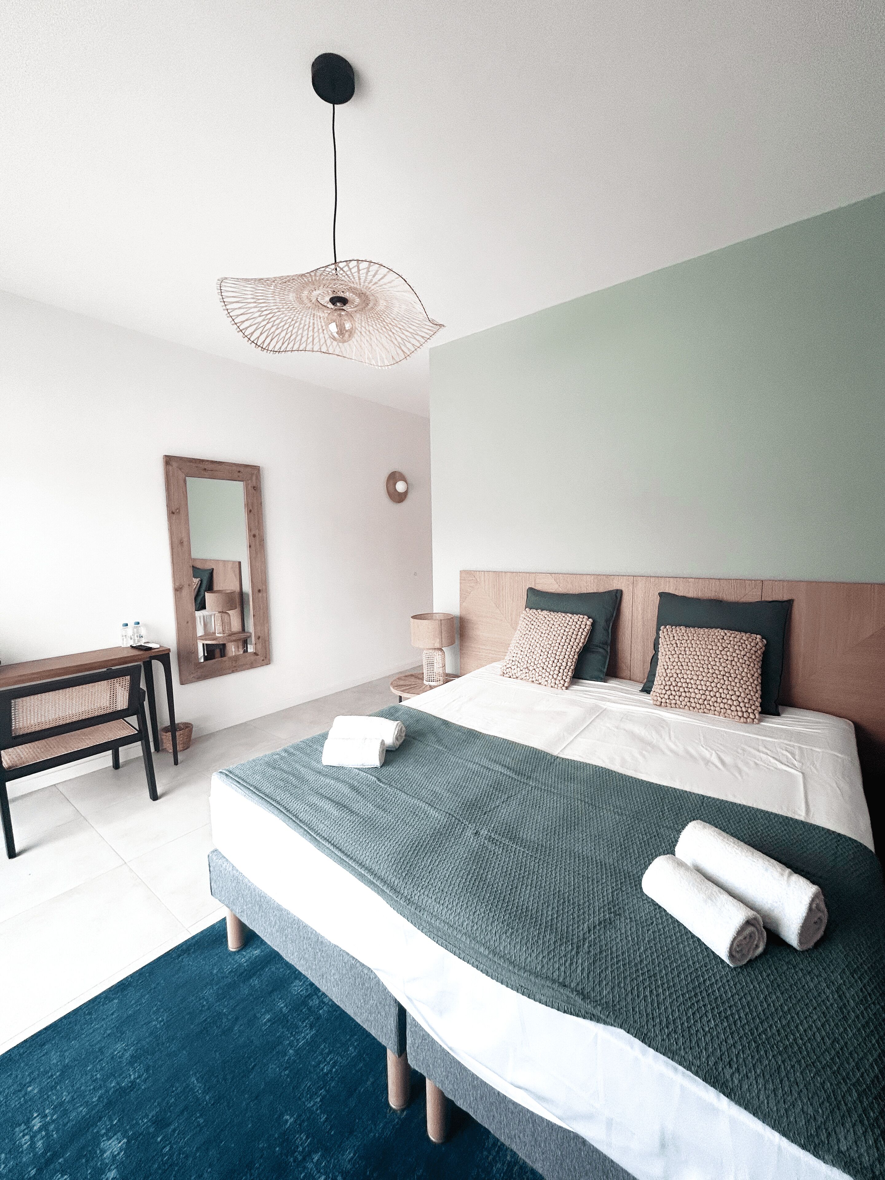 A modern bedroom with a large bed, a wooden nightstand, a desk, and a mirror.