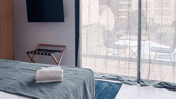 A bedroom with a bed, a TV mounted on the wall, a window with a view of the outside, and a chair by the window.