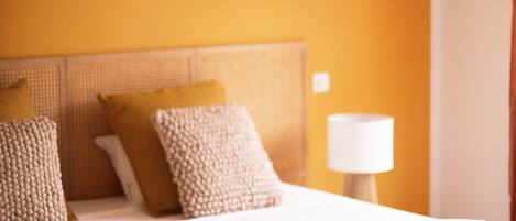 A neatly made bed with rolled towels, a bedside lamp, and a headboard with a woven texture.