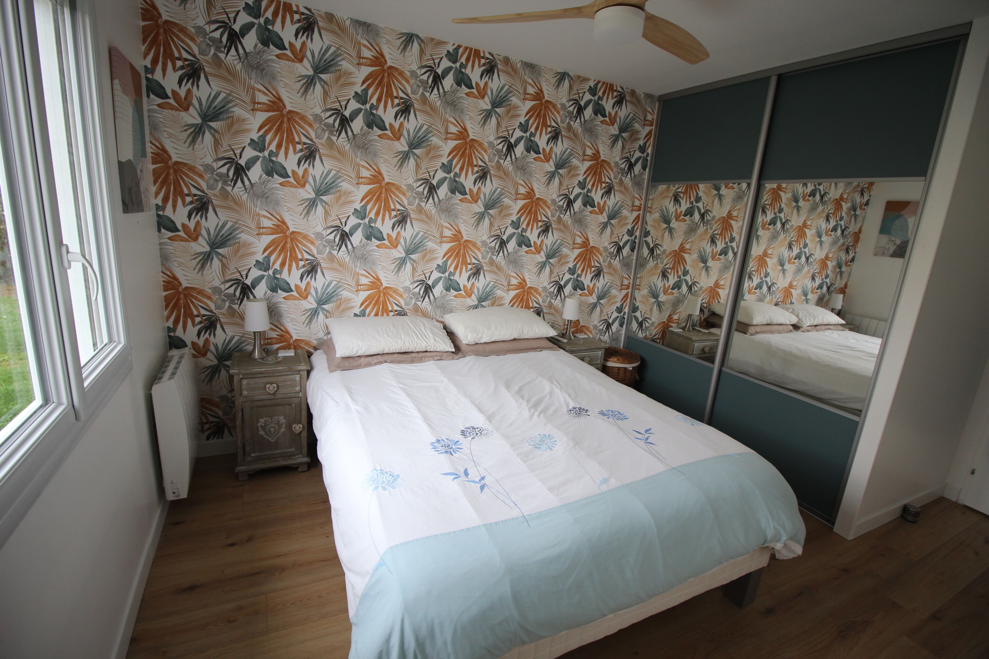 Una camera da letto con un letto, un comodino, una lampada, uno specchio e una finestra.
