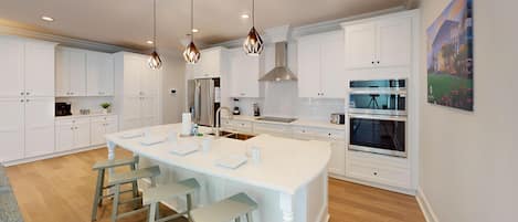 Une cuisine moderne avec des meubles blancs, un îlot central doté de tabourets, des appareils en acier inoxydable et un éclairage suspendu.