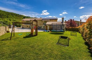 A house with a well-maintained lawn, a swing set, a trampoline, and a stone wall.