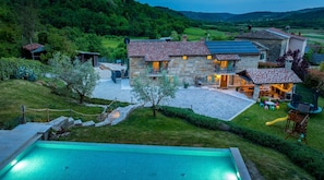 A stone house with a swimming pool, outdoor seating, and a view of the surrounding landscape.