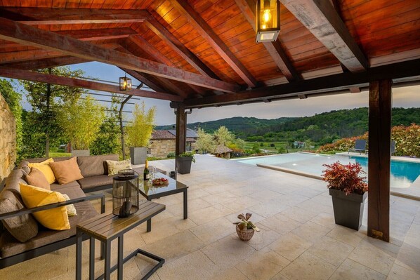A covered outdoor area with a pool, seating, and potted plants.