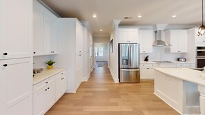 A modern kitchen with white cabinetry, a stainless steel refrigerator, and a wooden floor. - Saw Mill Sunset Beach, NC | Saw Mill 90 - 8 B (Sunset Beach)
