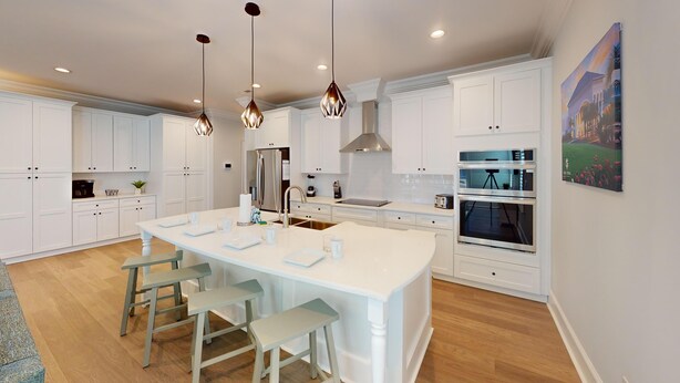 A modern kitchen with white cabinetry, a central island with stools, stainless steel appliances, and pendant lighting. - Saw Mill Sunset Beach, NC | Saw Mill 90 - 9 D (Sunset Beach)