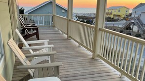 A wooden deck with lounge chairs, a railing, and a view of the ocean and buildings. - Toes in the Sand - Ocean Views, Steps from Beach (Oak Island)