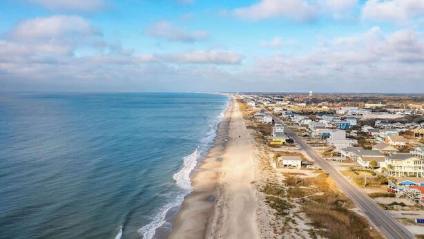 An aerial view of a coastal town with a beach, houses, and a road. - Toes in the Sand - Ocean Views, Steps from Beach (Oak Island)