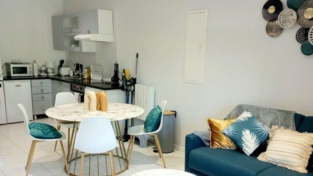 A modern living room with a blue sofa, white round coffee table, and a dining area with a white table and chairs. - Vue Exceptionnelle : 2 Pièces sur le Port de St-goustan (Auray)