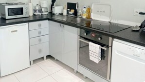 A modern kitchen with white cabinetry, a black countertop, and stainless steel appliances including a microwave, toaster, and dishwasher. - Vue Exceptionnelle : 2 Pièces sur le Port de St-goustan (Auray)