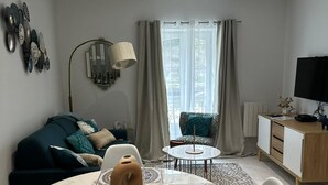 A modern living room with a sofa, a dining table with chairs, a TV, and a window with curtains. - Vue Exceptionnelle : 2 Pièces sur le Port de St-goustan (Auray)