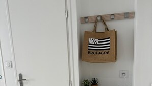 A white door with a handle, a small shelf with two potted plants, a hanging bag with 'BRETAGNE' text, and a decorative umbrella on the floor. - Vue Exceptionnelle : 2 Pièces sur le Port de St-goustan (Auray)