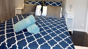 A neatly made bed with a blue and white patterned bedspread, two pillows, and a rolled towel. - Vue Exceptionnelle : 2 Pièces sur le Port de St-goustan (Auray)