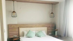 A bedroom with a wooden headboard, a bed with white linens, two green pillows, and two hanging light fixtures. - CALİSTO 17 BUTİK OTEL (Bozcaada)
