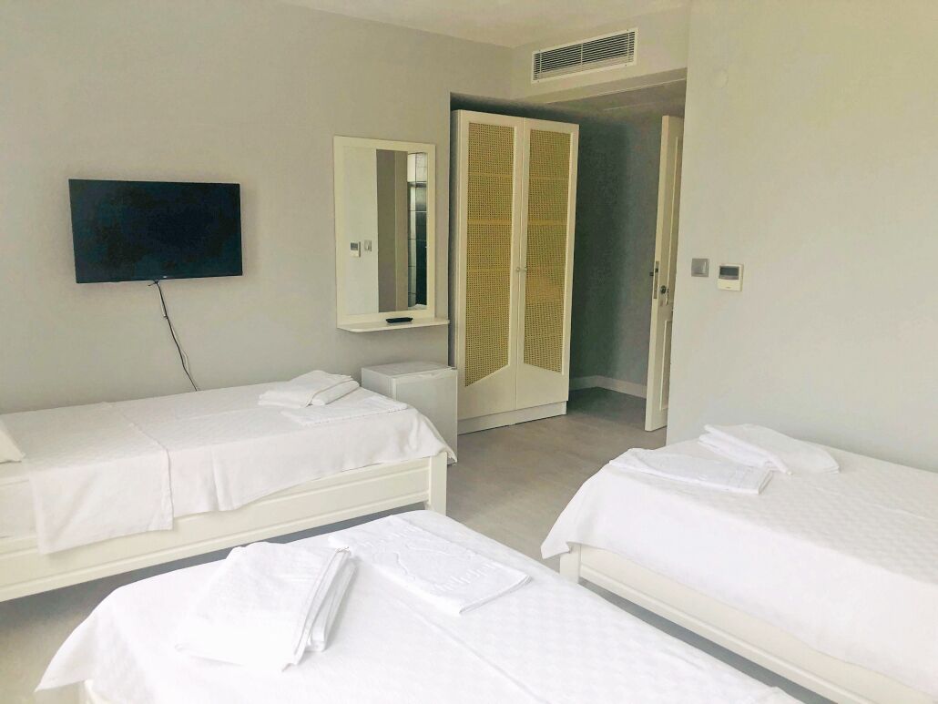 A hotel room with two single beds, a flat-screen TV mounted on the wall, a mirror, and a wardrobe with a louvered door.