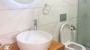 A modern bathroom with a round mirror, a white sink, and a toilet. - CALİSTO 17 BUTİK OTEL (Bozcaada)