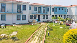 A courtyard with a paved walkway, outdoor seating, and a building with blue accents and stone walls. - CALİSTO 17 BUTİK OTEL (Bozcaada)