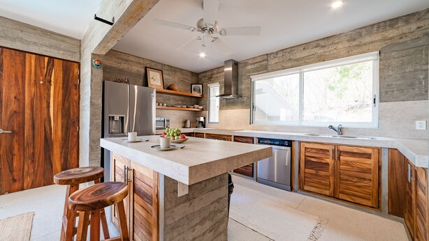 A modern kitchen with a large island, wooden cabinetry, and a built-in dishwasher. - Modern Condo In Walking Distance to Surf Beach (Bahias de Huatulco)