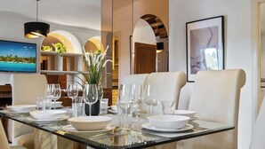 Un coin repas avec une table en verre, dressée pour quatre personnes, entourée de chaises rembourrées.