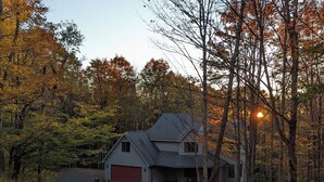 A two-story house with a red garage door, surrounded by trees with autumn foliage. - Lovely mountain home in a beautiful wooded setting. Welcome to Hart's Horn! (Davis)