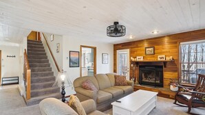 A cozy living room with a fireplace, a staircase, and a wooden wall. - Lovely mountain home in a beautiful wooded setting. Welcome to Hart's Horn! (Davis)