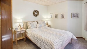 A bedroom with a wooden bed, two bedside tables with lamps, a wall-mounted wreath, and framed artwork on the wall. - Lovely mountain home in a beautiful wooded setting. Welcome to Hart's Horn! (Davis)