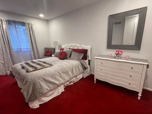 A bedroom with a bed, a dresser, a mirror, and a window with curtains.