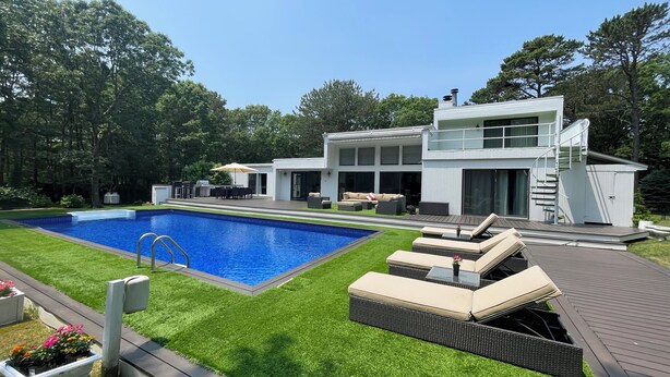 Une maison moderne dotée d’une piscine, de mobilier d’extérieur et d’une pelouse bien entretenue.