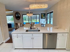 A kitchen with a central island, stainless steel dishwasher, and a chandelier.