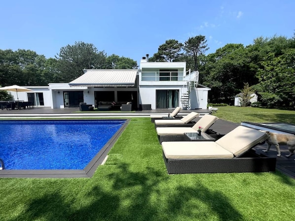 A modern house with a swimming pool, outdoor seating, and a dog.