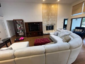 Ein modernes Wohnzimmer mit einem weißen Ledersofa, einem roten Hocker, einem Flachbildfernseher und einem Kamin.