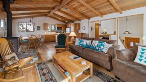 Ein geräumiges Wohnzimmer mit Holzboden, einem braunen Sofa mit gemusterten Kissen, einem Holztisch und einem Schaukelstuhl.