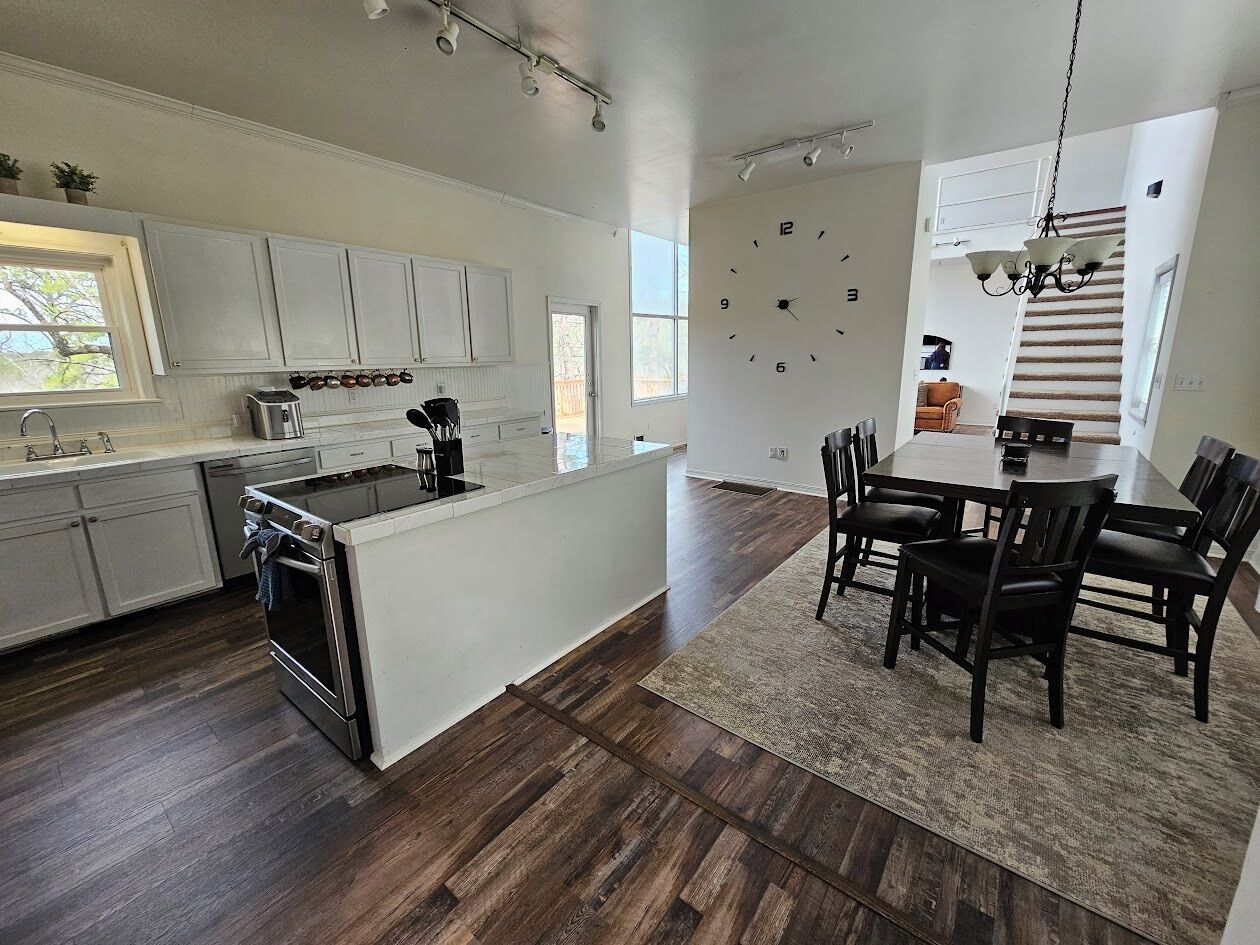 A modern kitchen with a central island, dark wood flooring, and a dining area with a large table and chairs.