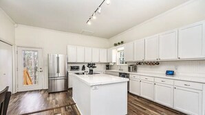 A modern kitchen with white cabinetry, a stainless steel refrigerator, and a wooden floor. - Eureka Springs getaway 2 acres in the center of town, super close to historic DT (Eureka Springs)