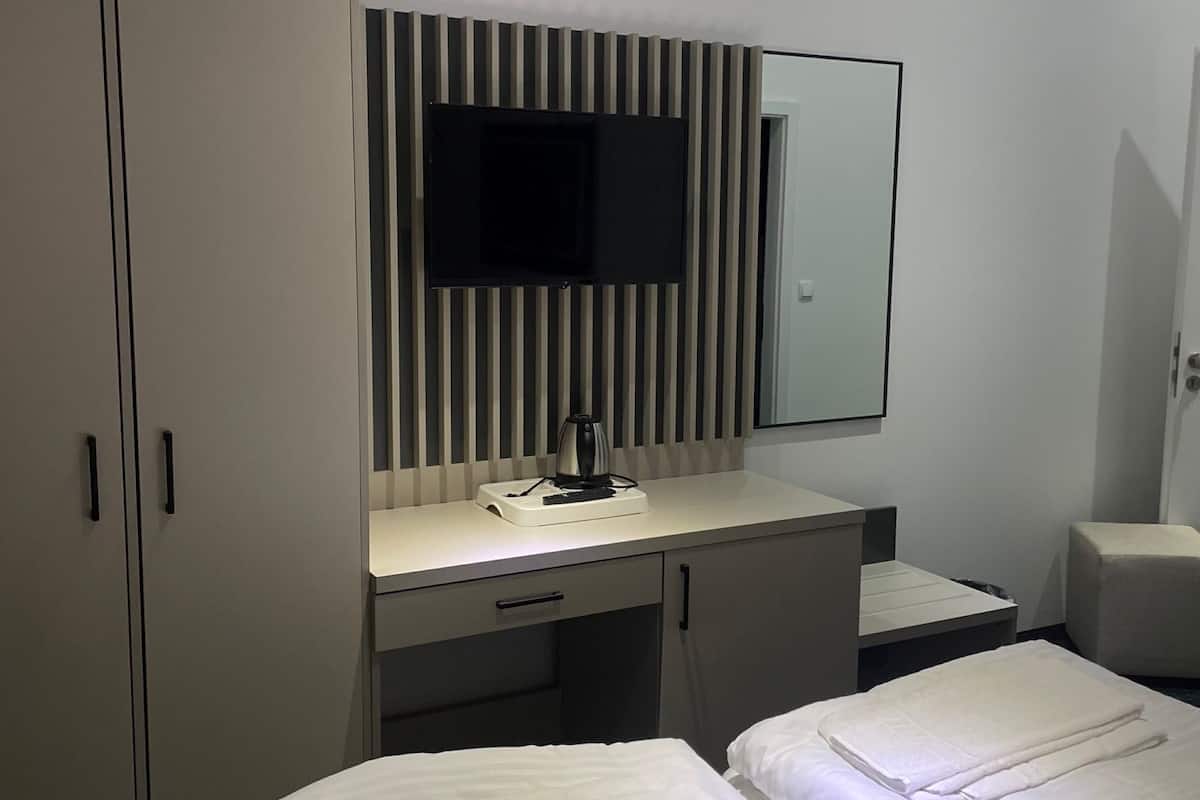 Quarto de hotel com duas camas, uma escrivaninha, televisão de tela plana, espelho e guarda-roupa.