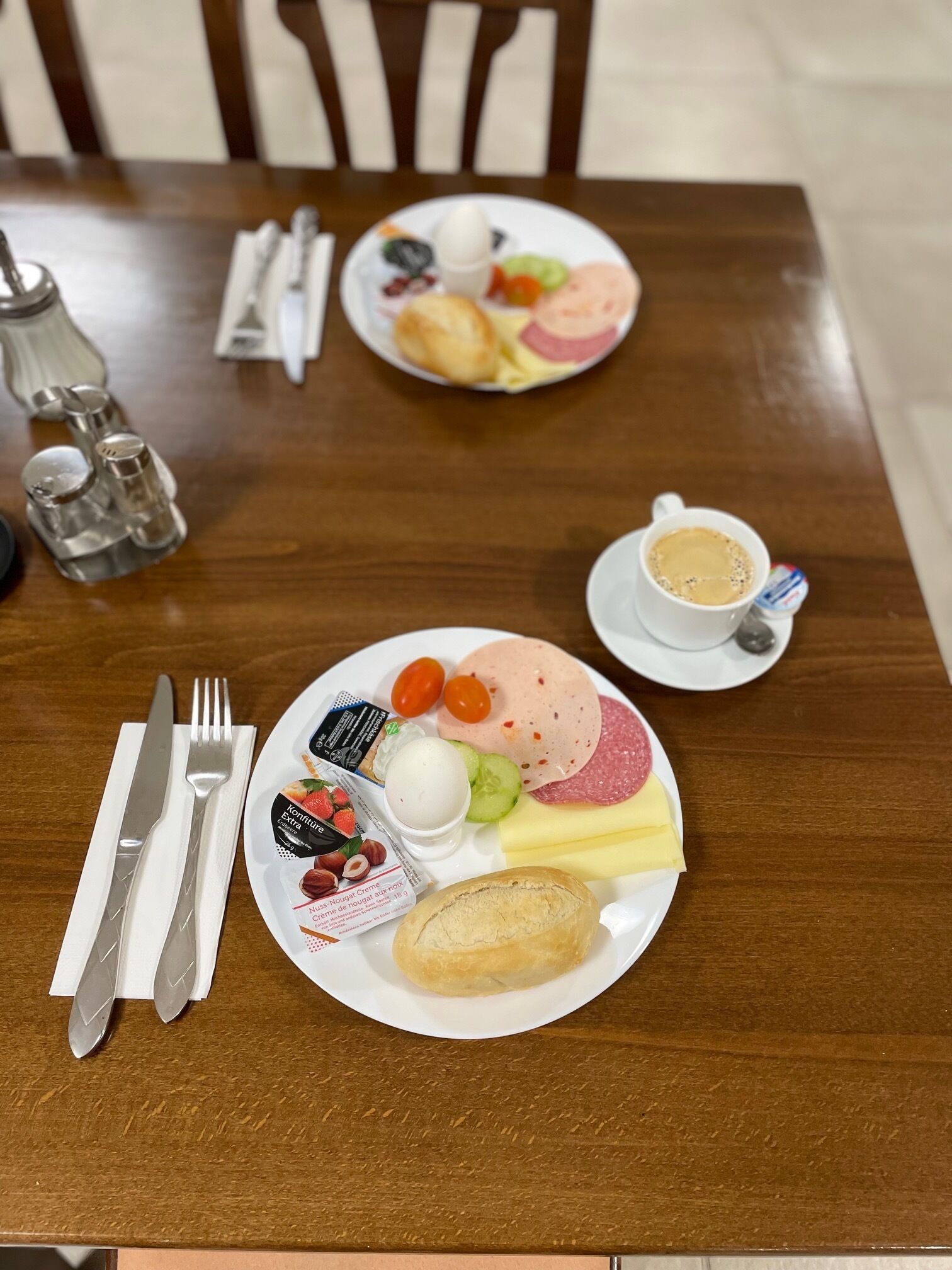 Uma mesa de jantar de madeira com pratos de comida, uma xícara de café e talheres.