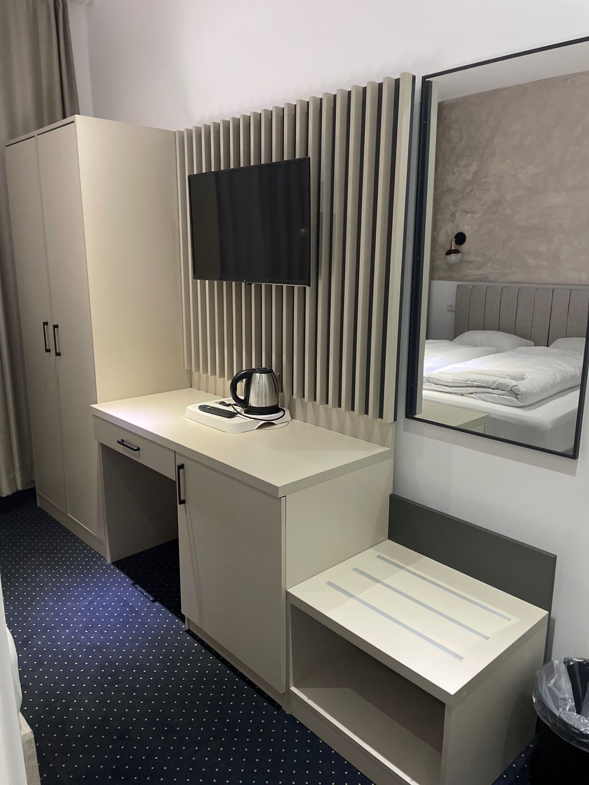 Una habitación de hotel con cama, escritorio con hervidor, espejo y armario.
