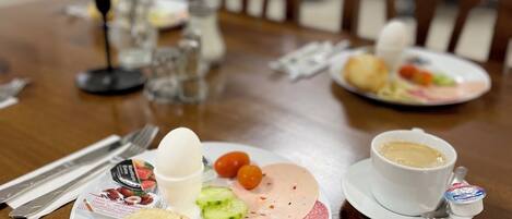 A dining table with plates of food, a cup of coffee, and a small container of yogurt.