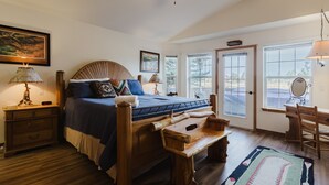 Une chambre à coucher avec un lit en bois, des tables de chevet, un bureau et une chaise. On y trouve des fenêtres, un ventilateur de plafond et une porte.