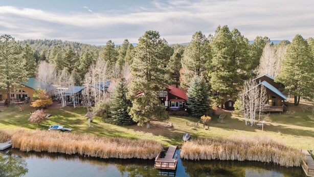 Un chalet au bord du lac, doté d’un quai, entouré d’une forêt dense et surplombant un ciel dégagé.