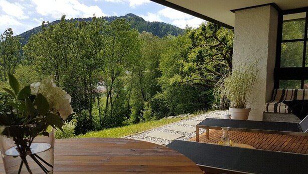 En træterrasse med udendørs møbler, en potteplante og udsigt til et bjerrelandskab.