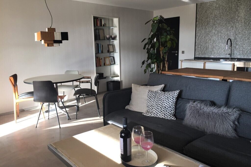 Ein modernes Wohnzimmer mit einer Couch, einem Esstisch mit Stühlen, einem Bücherregal und einer Küchenzeile mit Spüle.