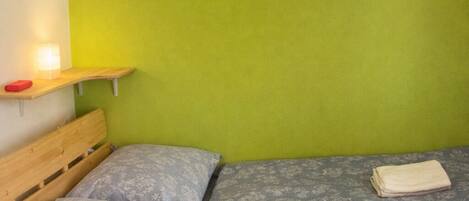 A room with a bed, a wooden headboard, a green wall, and a small shelf with a lamp.